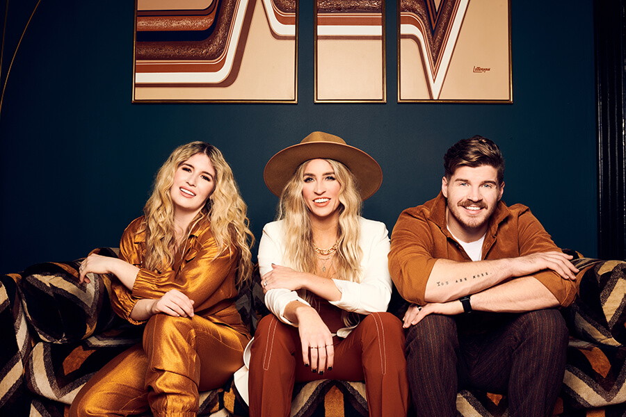 Two women and one man are smiling and sitting on a colourful sofa