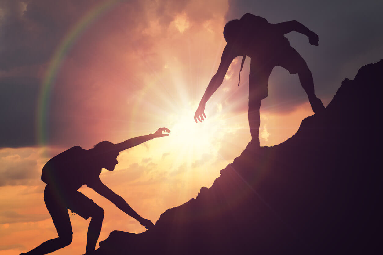Two people are climbing a mountain top with the sun going down