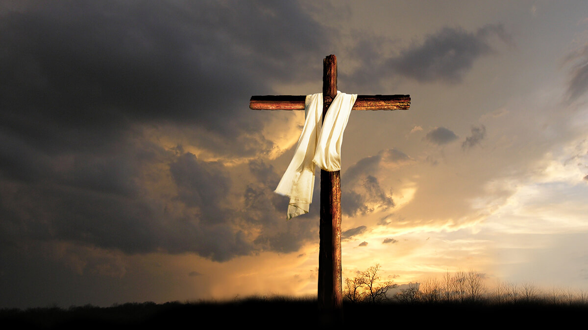 Cross, white material on it, sunset and dark clouds in the background