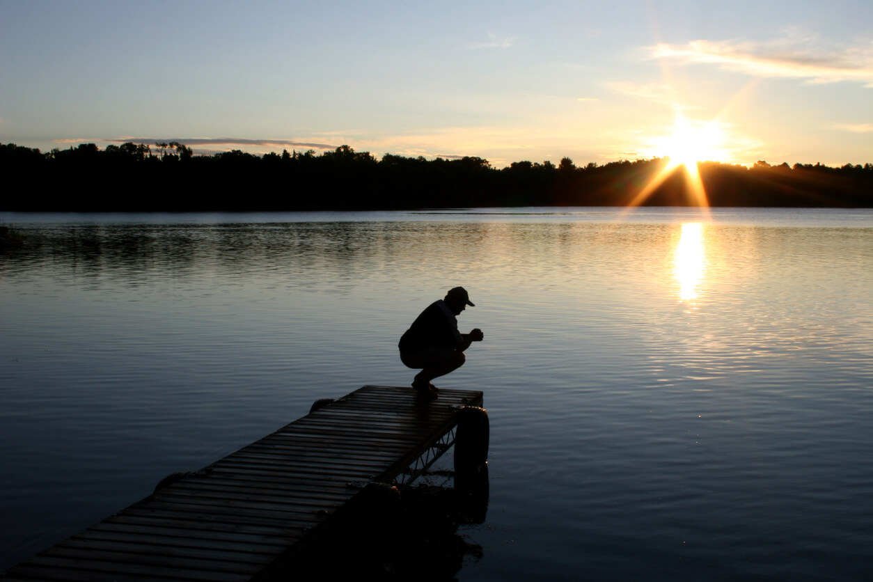 Crouching man on the pier, lake, and sunset in the background
