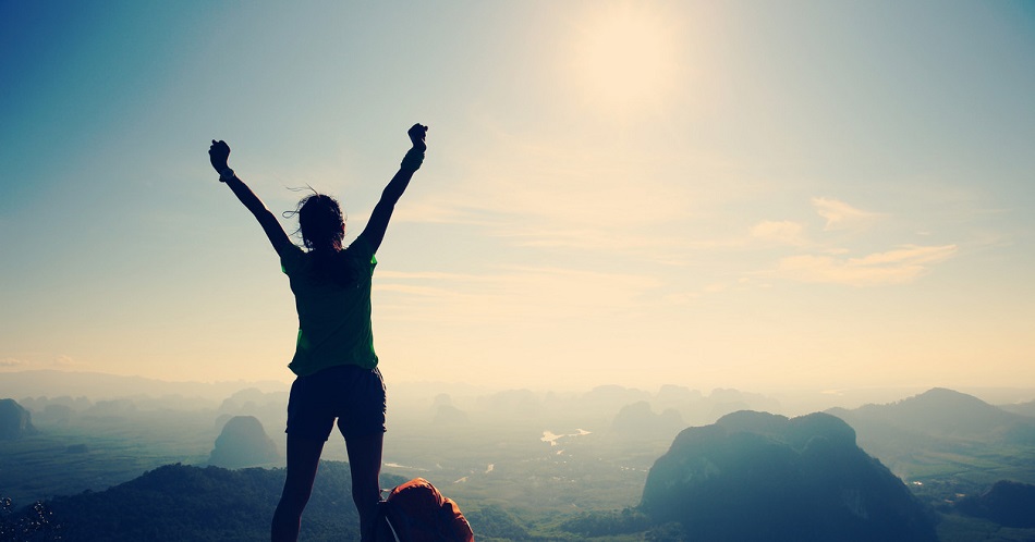 A woman standing on a mountaintop with her arms raised above her head