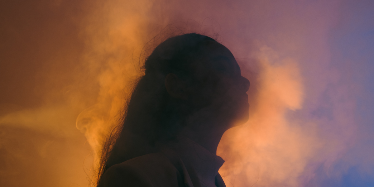 A dramatic profile view of the siloheutte of a woman in fog. The lighting is beautiful - with blue in front of her and orange behind.