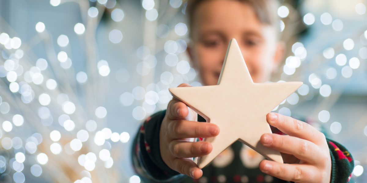 A young boy surrounded by Christmas lights is holding up a Christmas star box