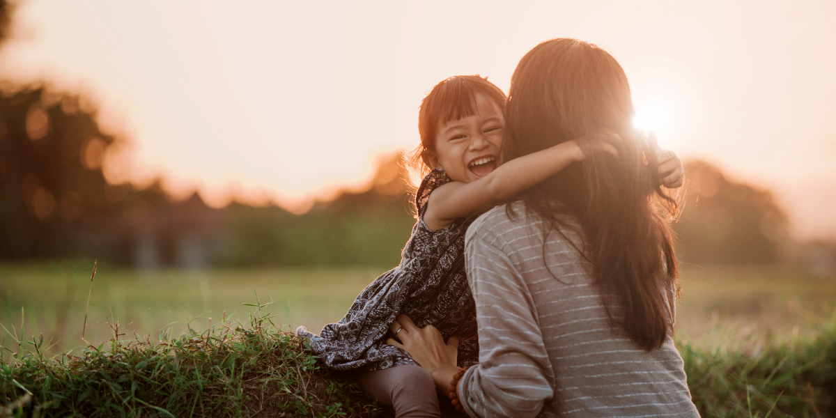 A little girl hugging her mom while smiling and laughing. They are outside during sunset