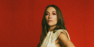 Lauren Daigle against a textured red background. She is wearing a beige tanktop