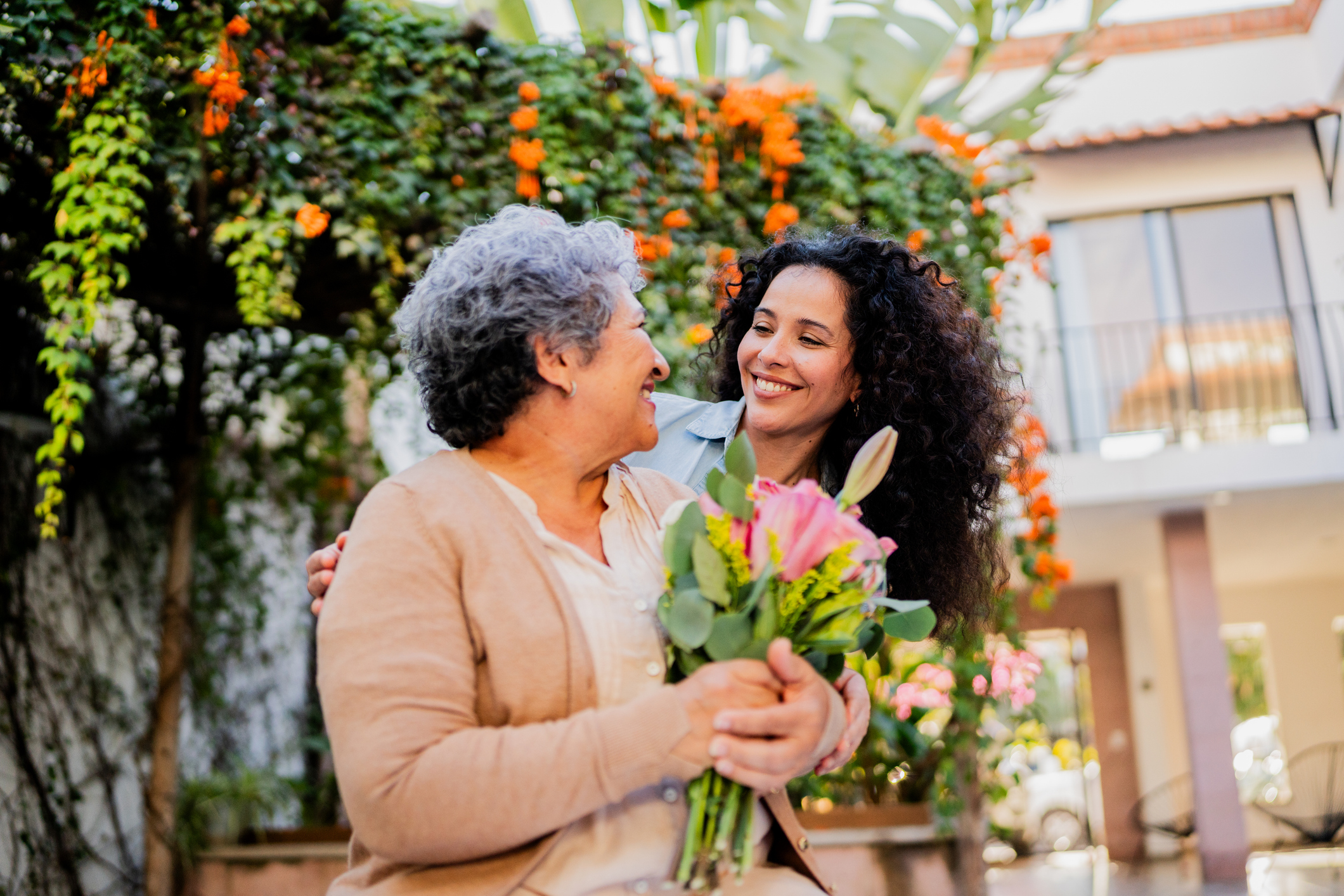 Mid adult woman embracing and giving flowers to mother outdoors