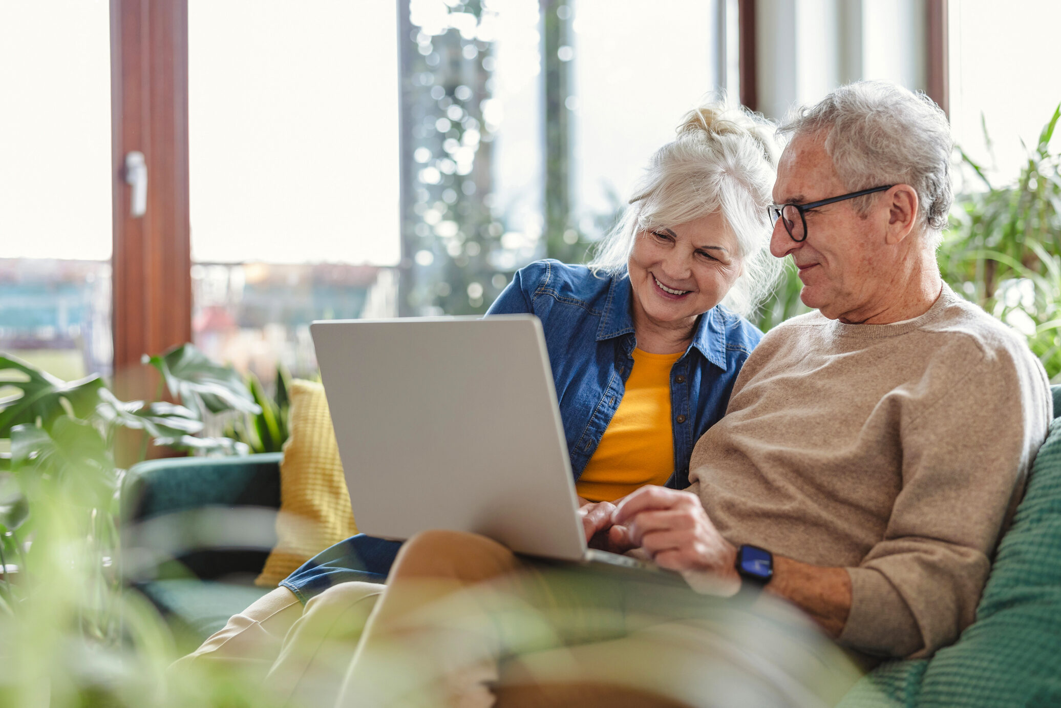 Senior couple using laptop while sitting on sofa in living room at home