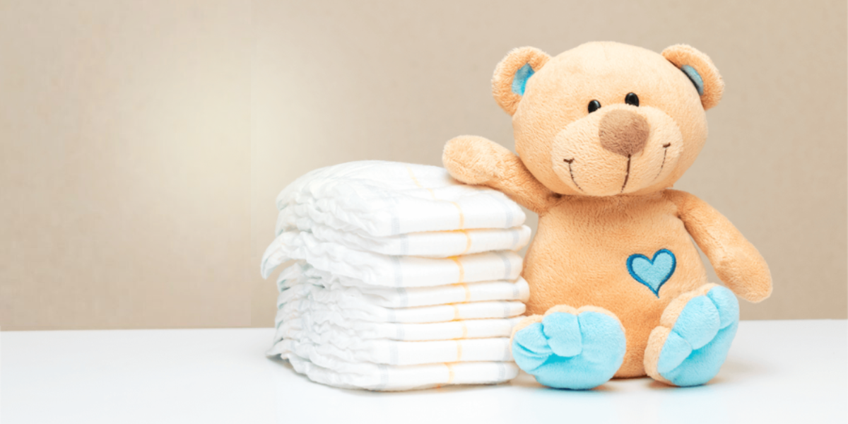 a stuffed teddy bear sitting next to a pile of clean diapers with its arm resting on top